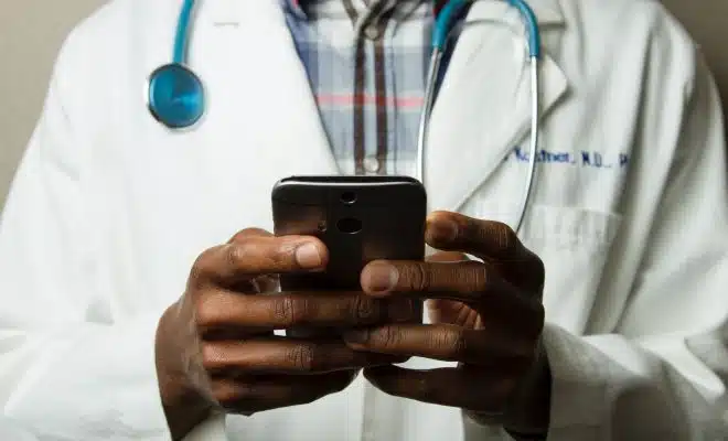 person wearing lavatory gown with green stethoscope on neck using phone while standing