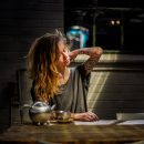 woman in gray top sitting beside gray tea pot and cup on brown wooden table